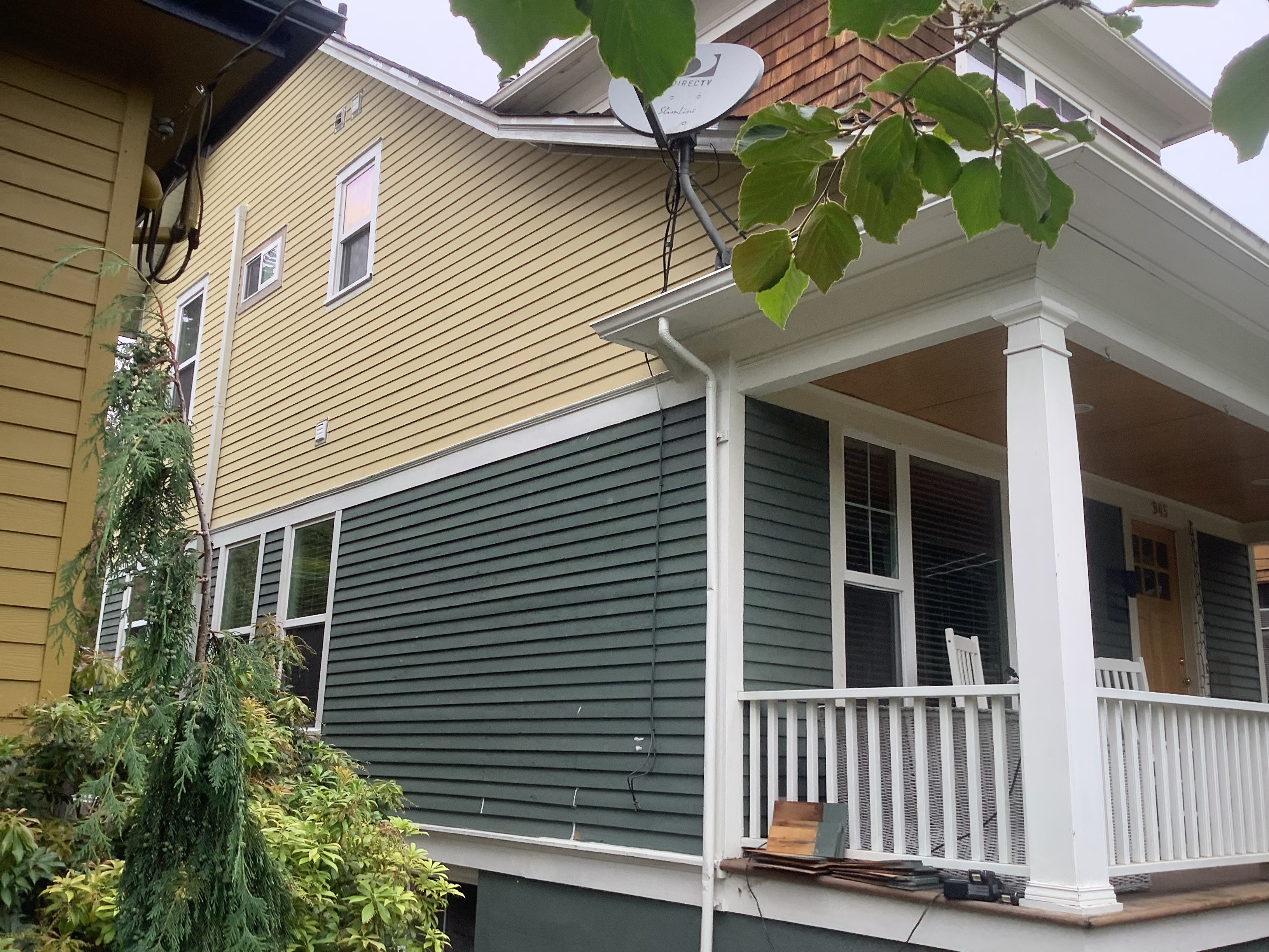 Yellow and green two-tone siding with a white porch before painting
